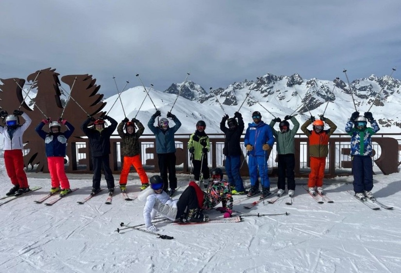 Pupils in skiwear pose in front of a snowy backdrop and a big sign saying Serre Chevalier